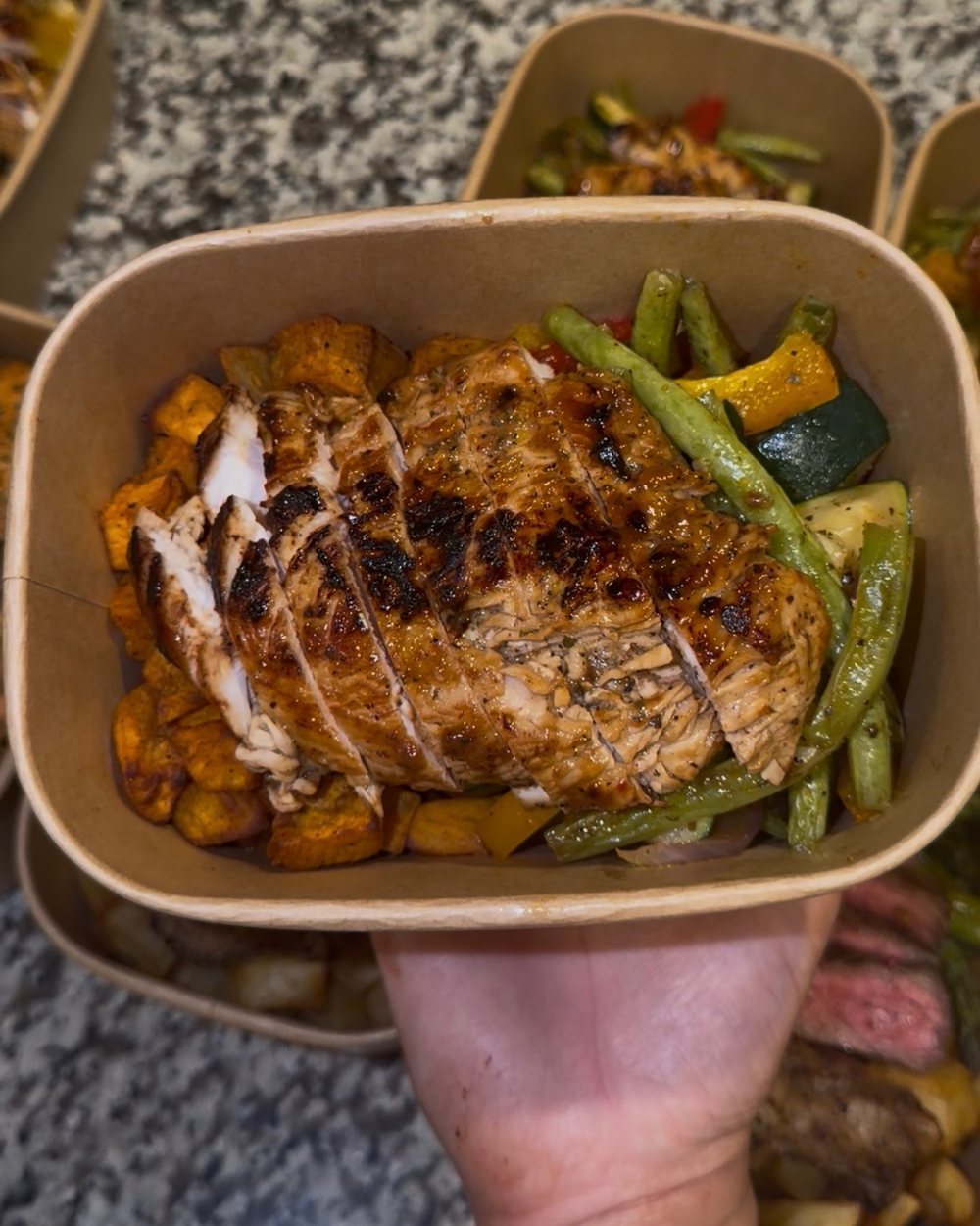 Makaela holding a Harvey Eats Co. meal: grilled chicken with sweet potatoes and green beans